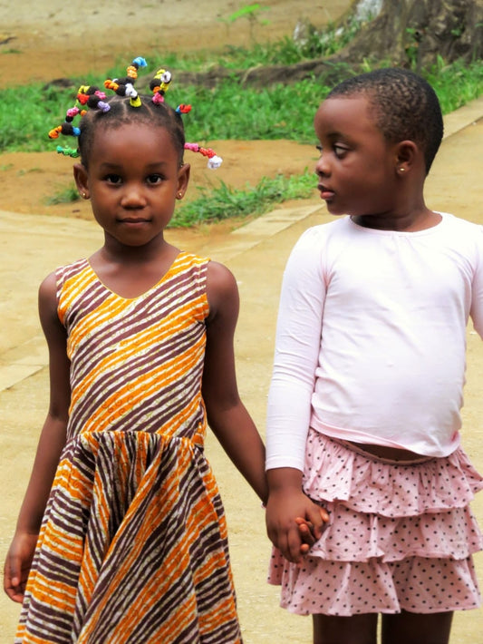 Cross Stitch | Abidjan - 2 Girls In White And Orange Dress Standing On Brown Sand During Daytime - Cross Stitched