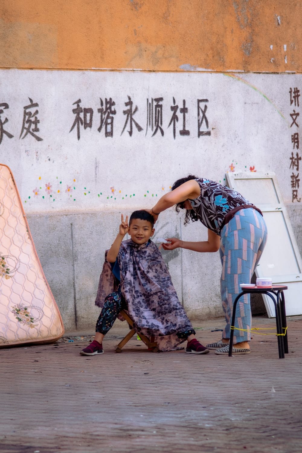 Cross Stitch | Dalian - Boy Sitting On Stool Beside Standing Woman Near Wall - Cross Stitched