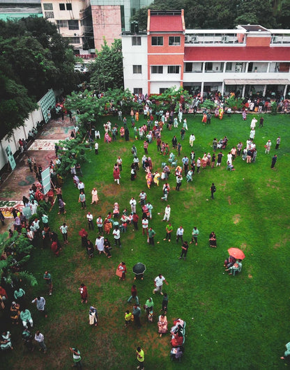 Cross Stitch | Dhaka - Aerial Photography Of People Walking On Green Field Near White And Red Concrete 3-Story Building During Daytime - Cross Stitched