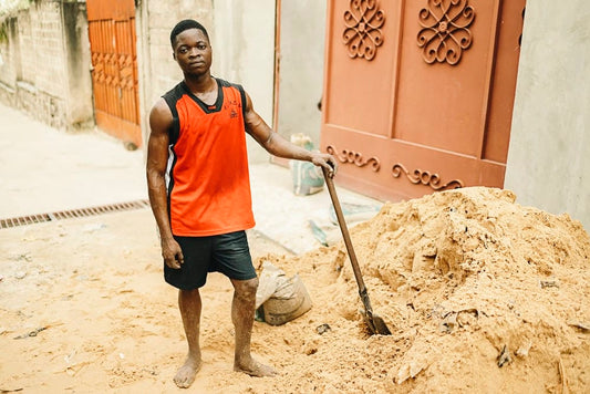 Cross Stitch | Kinshasa - Man In Red Tank Top And Black Shorts Holding Shovel - Cross Stitched