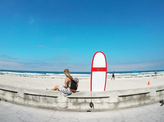 Cross Stitch | San Diego - Woman Sitting On White Concrete Barrier Beside Skimboard During Daytime - Cross Stitched