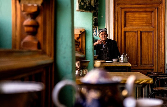 Cross Stitch | Ürümqi - Man Sitting In Front Of Table Near Door - Cross Stitched